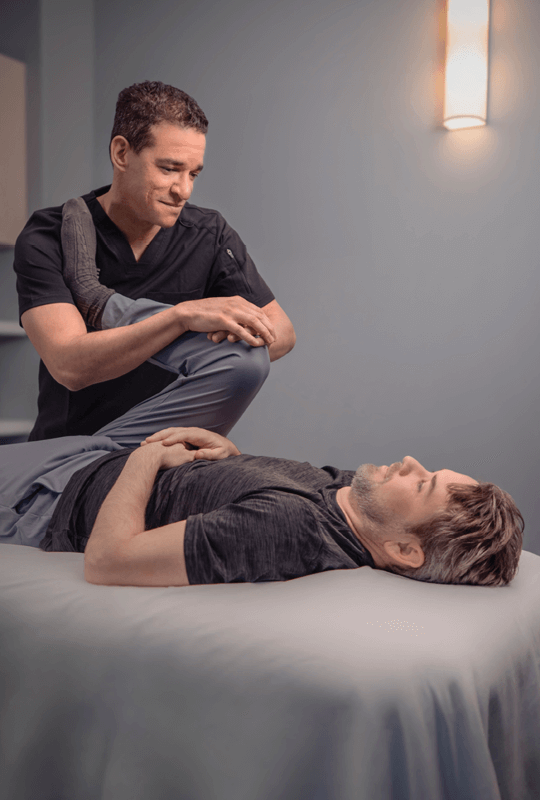 Man lying on table as therapist performs a stretch on the man's leg. 