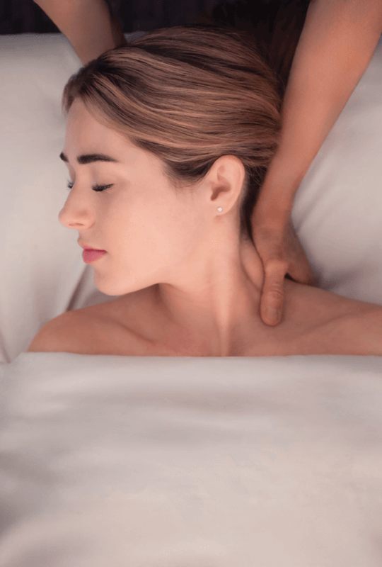 Woman relaxing as a therapist massages her neck. 