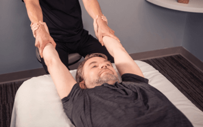 Man lying on table as therapist performs stretch. 