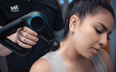 Woman relaxes at massage gun is moved along her shoulders. 