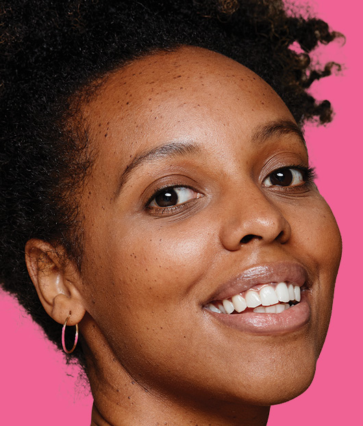 Close-up of smiling woman's face in front of a light pink background. 