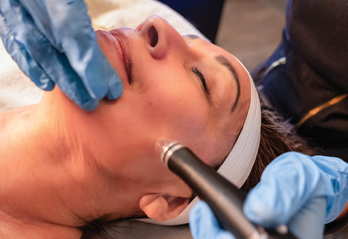 Woman with her eyes closed as she receives a hydrafacial treatment from an esthetician. 