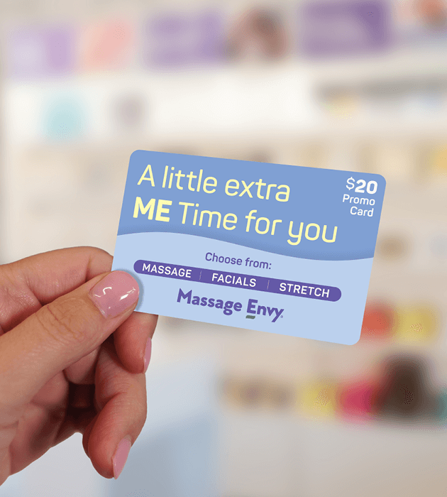 Close-up of a hand holding a Massage Envy promo card worth $20. 