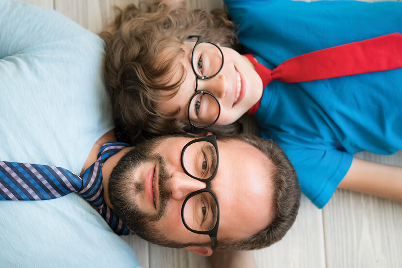 Father and son with glasses and neckties on smile as they lie on the floor. 