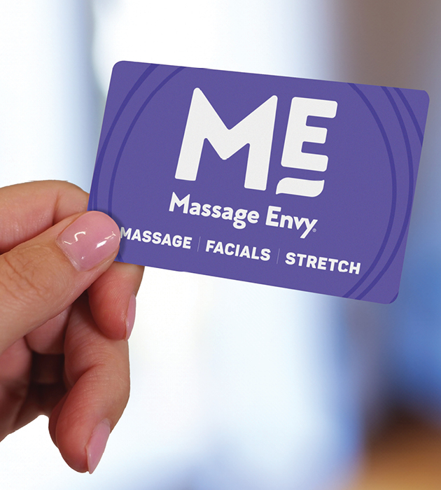 Close-up of a woman's hand holding a Massage Envy gift card. 